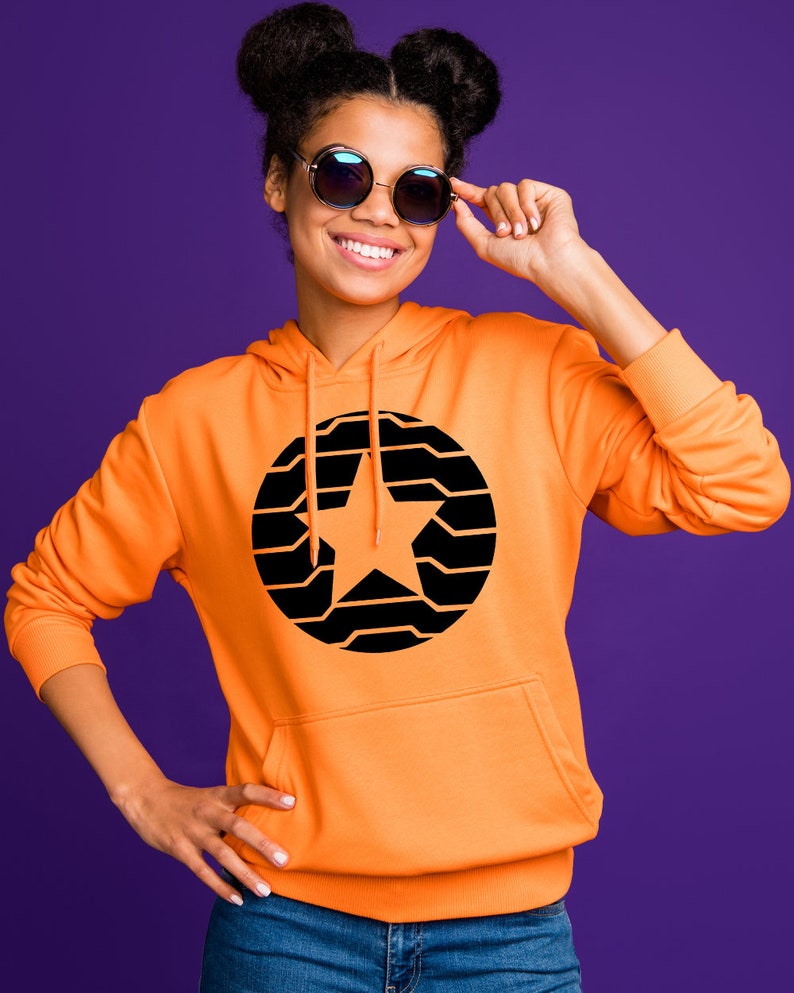 K&ouml;nnte beinhalten: Ein orangefarbener Kapuzenpullover mit einem schwarzen und orangefarbenen Sterndesign. Der Kapuzenpullover hat eine Vordertasche und eine Kapuze. Die Person auf dem Bild tr&auml;gt eine runde Sonnenbrille und l&auml;chelt. Der Hintergrund ist einfarbig lila.