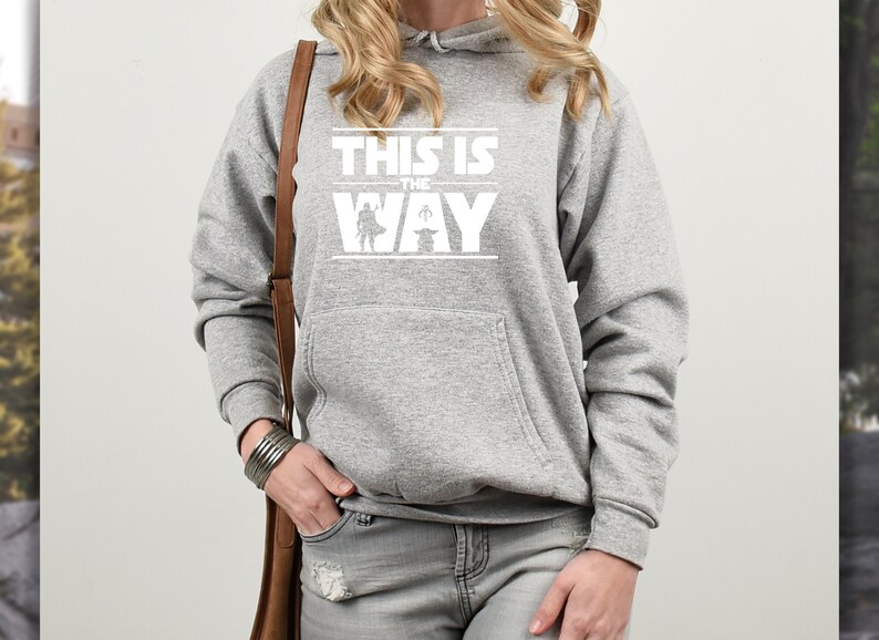 Puede incluir: Una sudadera con capucha gris con un bolsillo delantero y texto blanco que dice "THIS IS THE WAY" con un gr&aacute;fico de un personaje y un beb&eacute;. La sudadera es de estilo casual.