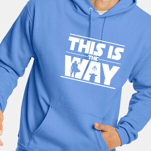 Puede incluir: Sudadera con capucha azul claro con un gr&aacute;fico blanco que dice "THIS IS THE WAY". El gr&aacute;fico incluye siluetas de un personaje y una criatura peque&ntilde;a. La sudadera tiene un bolsillo delantero y una capucha con cord&oacute;n.