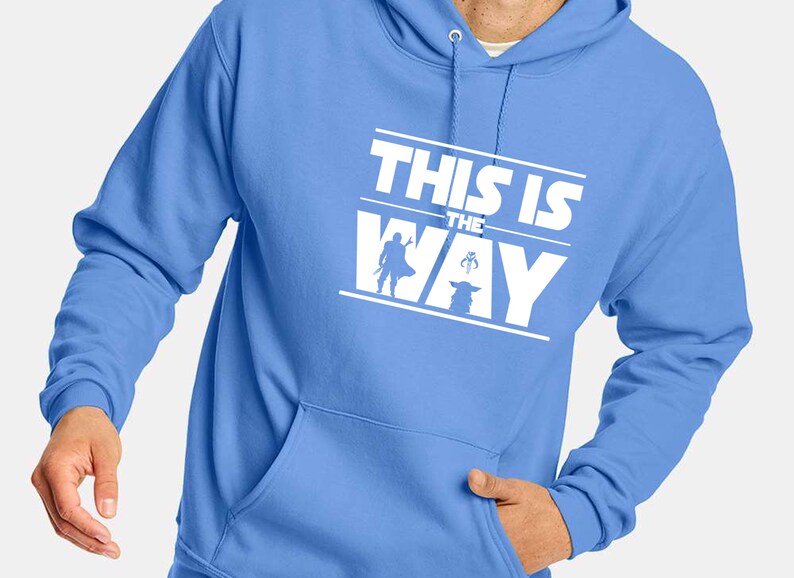 Puede incluir: Sudadera con capucha azul claro con un gr&aacute;fico blanco que dice "THIS IS THE WAY". El gr&aacute;fico incluye siluetas de un personaje y una criatura peque&ntilde;a. La sudadera tiene un bolsillo delantero y una capucha con cord&oacute;n.