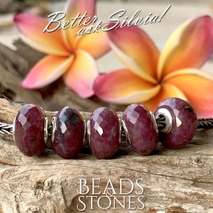Pode incluir: Cinco contas de pedras preciosas vermelhas escuras facetadas com detalhes prateados são exibidas em uma superfície de madeira. As contas são enfiadas juntas, e a imagem inclui o texto "BEADS & STONES" e "Better ask Silvia!"