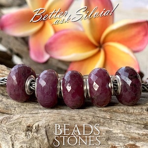 May include: Five faceted, deep red gemstone beads with silver accents are strung together. The beads are displayed on a wooden surface, with the text "BEADS & STONES" at the bottom. A blurred flower is in the background, with the text "Better, Silvia! ask" at the top.