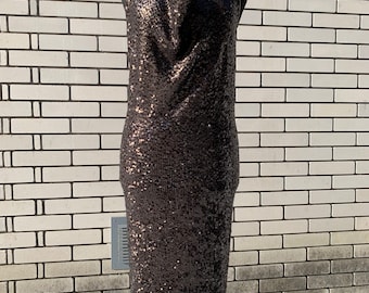 Puede incluir: Un vestido negro de tirantes con cuello de pico y tejido de lentejuelas. El vestido es de largo midi y tiene una silueta ajustada.