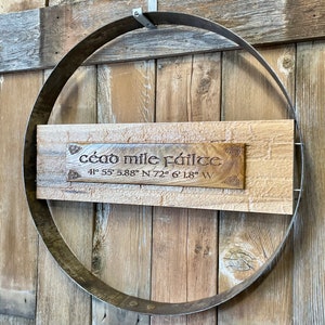 May include: A wooden sign with the text "céad mile fáilte" and coordinates "41° 55' 5.88" N 72° 6' 1.8" W" hanging on a rustic wooden wall.