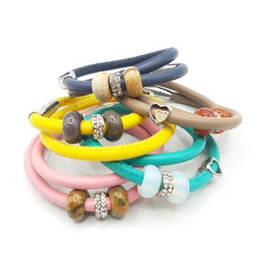 Peut inclure: Un ensemble de bracelets en cuir colorés avec des perles et des breloques décoratifs. Les bracelets sont dans des tons de jaune, rose, bleu et marron.
