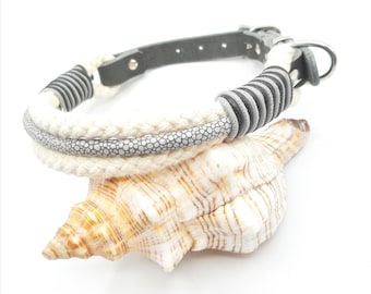 Op de afbeelding: Een hondenhalsband met een wit touwontwerp, geaccentueerd met grijze en zwarte details. De halsband heeft een grijze leren riem en een metalen sluiting. De halsband ligt op een zeeschelp.