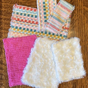 May include: An assortment of colorful washcloths and cloths. The washcloths feature patterns of stripes and dots in shades of pink, blue, yellow, and green. Two white, fluffy cloths and a bright pink cloth are also included.