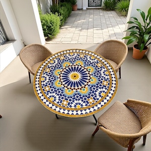 May include: A round table with a colorful mosaic tile top featuring a geometric star pattern in shades of blue, yellow, and white, supported by a black metal frame, accompanied by three woven chairs with light brown seats and wooden legs.