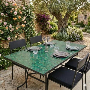 May include: A green mosaic-tiled outdoor dining table with a black metal frame, set with plates, glasses, and silverware. Four black chairs with cushions surround the table. The scene is set in a garden with a stone wall and climbing roses.