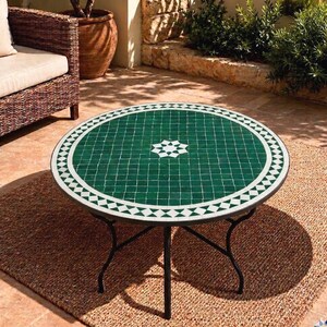 Peut inclure: Une table ronde avec un plateau en mosaïque verte orné d'une bordure géométrique blanche et d'une étoile centrale blanche. La table repose sur un cadre en métal noir doté de quatre pieds incurvés qui se rejoignent au centre sous le plateau.