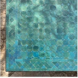 May include: Close-up of a mosaic table top with a teal and turquoise color scheme. The mosaic tiles are arranged in a geometric pattern, with a border of smaller tiles. The table has a weathered appearance.
