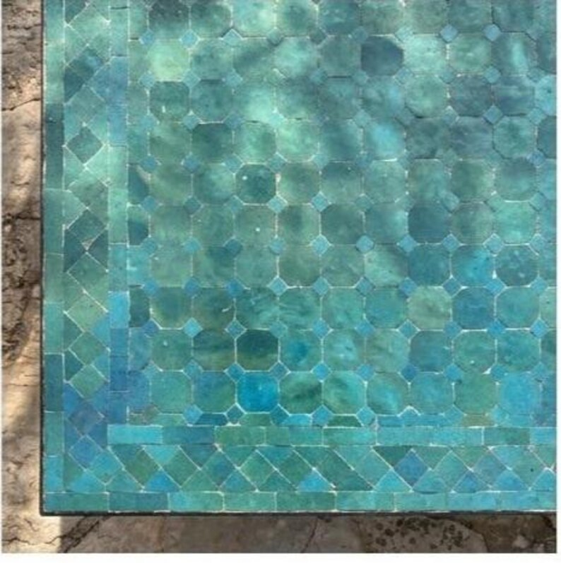 May include: Close-up of a mosaic table top with a teal and turquoise color scheme. The mosaic tiles are arranged in a geometric pattern, with a border of smaller tiles. The table has a weathered appearance.