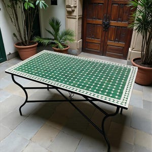 Peut inclure: Une table rectangulaire dotée d'un plateau en mosaïque verte et blanche avec un motif géométrique. La table est soutenue par un cadre en métal noir avec quatre pieds incurvés et une structure en croix reliant les pieds pour la stabilité.