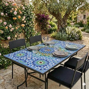 Peut inclure: Une table de salle à manger extérieure rectangulaire avec un plateau en mosaïque géométrique bleue, verte et blanche et un cadre en métal noir. Elle est accompagnée de quatre chaises en métal noir avec des coussins noirs, dressée avec des assiettes.
