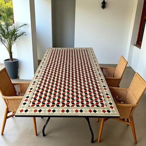 May include: A rectangular outdoor dining table with a mosaic tile top featuring a geometric pattern in red, black, and cream. The table is supported by black metal legs and is surrounded by four wicker chairs. A potted palm tree is visible in the background.