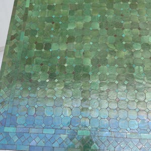 May include: Overhead view of a tiled surface with a gradient of green and blue hues. The tiles are arranged in a repeating geometric pattern of octagons and squares, with small diamond-shaped accents. The overall effect is a mosaic-like design.