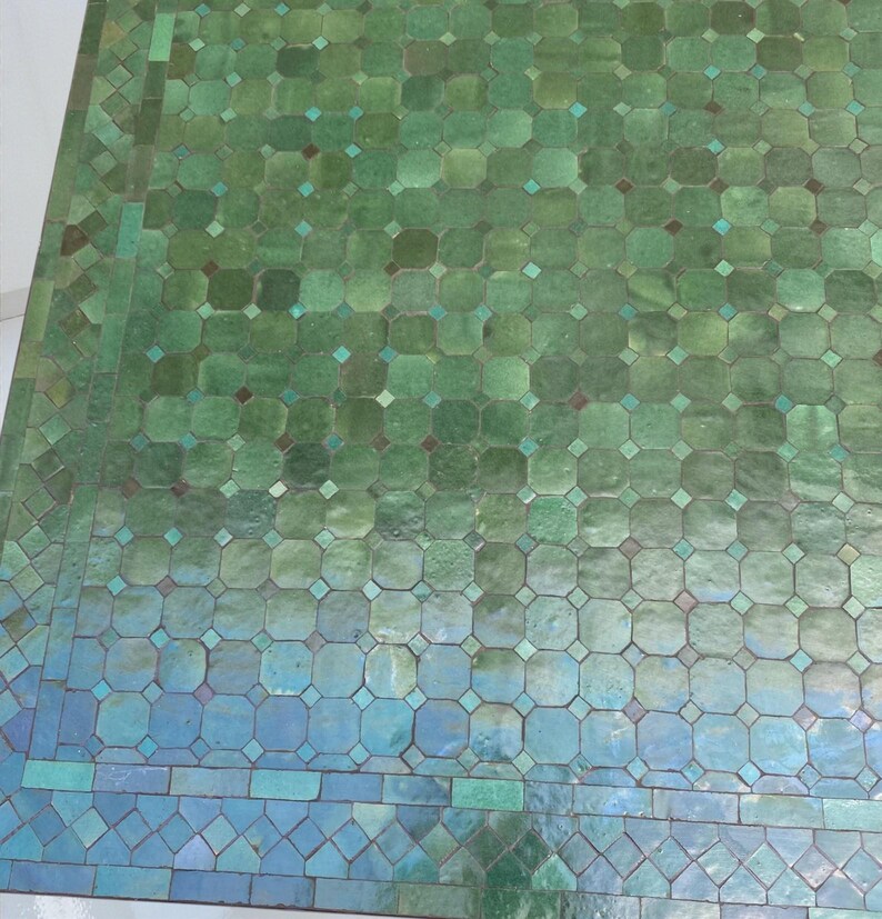 May include: Overhead view of a tiled surface with a gradient of green and blue hues. The tiles are arranged in a repeating geometric pattern of octagons and squares, with small diamond-shaped accents. The overall effect is a mosaic-like design.