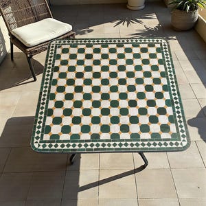 Peut inclure: Une table carrée dotée d'un plateau en mosaïque avec un motif géométrique répétitif en vert foncé, blanc et jaune moutarde. Le plateau est bordé d'une frise en losanges et repose sur un cadre en métal noir avec quatre pieds.