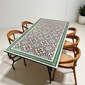 May include: A rectangular outdoor dining table with a mosaic tile top featuring a geometric pattern in shades of blue, green, brown, and white. The table is surrounded by six wicker chairs with wooden frames. The table's frame is black.