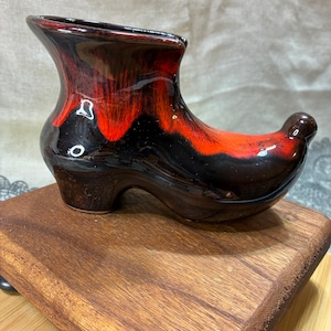 May include: A ceramic shoe-shaped planter with a glossy finish. The planter features a blend of red, black, and brown colors. The shoe has a high heel and a rounded toe, suitable for small plants or decorative items.