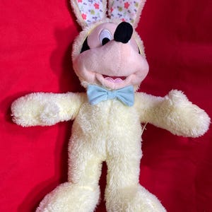 May include: Yellow plush Easter bunny costume with a blue bow tie. The bunny has Mickey Mouse ears and a black nose.