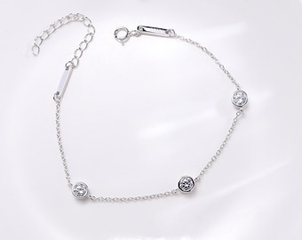 Puede incluir: Un brazalete de cadena de plata con tres pequeñas piedras redondas transparentes.