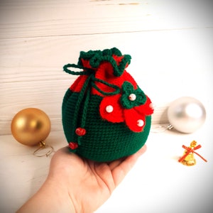 K&ouml;nnte beinhalten: Eine gr&uuml;ne und rote geh&auml;kelte Weihnachtsgeschenkt&uuml;te mit einer wei&szlig;en Perlenverzierung. Die Tasche ist mit einer gr&uuml;nen Schnur gebunden und hat einen gekr&auml;uselten oberen Rand.