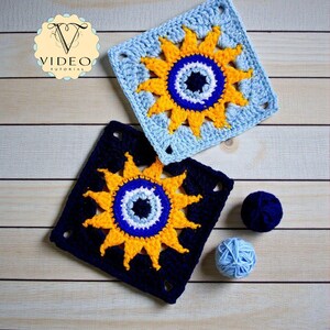May include: Two crocheted squares with a sunflower design. One square is light blue, the other is navy blue. The sunflowers have yellow petals and a blue and white center. Two balls of yarn are also visible.