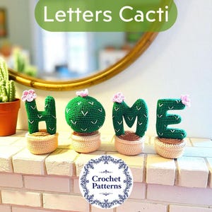 May include: Crocheted letters spelling "HOME" in green, cactus-shaped designs, each with a pink flower accent. The letters sit in beige crochet pots, displayed on a white brick surface. The image includes the text "Letters Cacti".