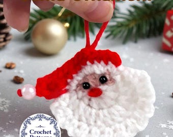 May include: A handmade crochet Santa ornament with a red hat and white beard. The ornament has black eyes, a red nose, and a pink bead on the side. The text "Santa Ornament" is at the top. The ornament is held by a hand.