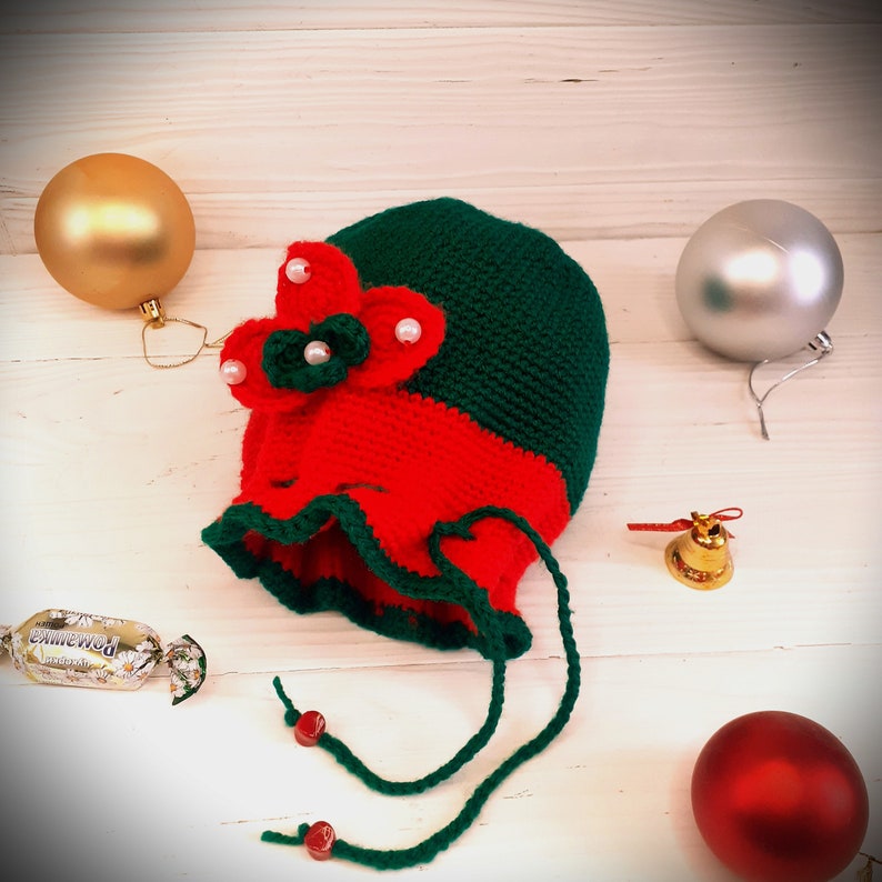 K&ouml;nnte beinhalten: Ein rot-gr&uuml;ner Weihnachtsstrumpf aus H&auml;kelarbeit mit einer wei&szlig;en Schleife und Perlen. Der Strumpf hat einen gr&uuml;nen Kordelzug und ist mit wei&szlig;en Perlen verziert.