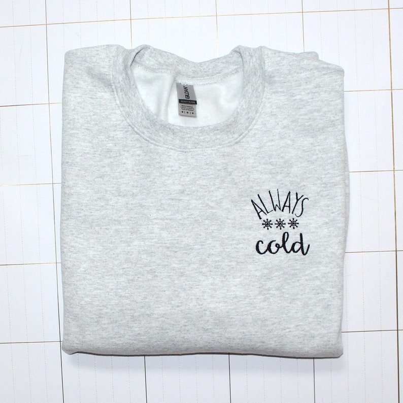 Pode incluir: Uma camisa de moletom cinza com o texto "ALWAYS *** cold" bordado na frente.