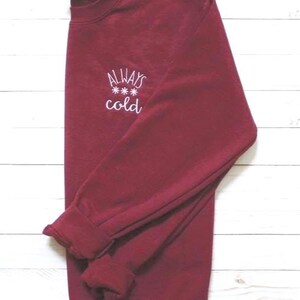 Pode incluir: Camisola de cor bord&ocirc; com texto bordado em branco que diz "ALWAYS *** cold".