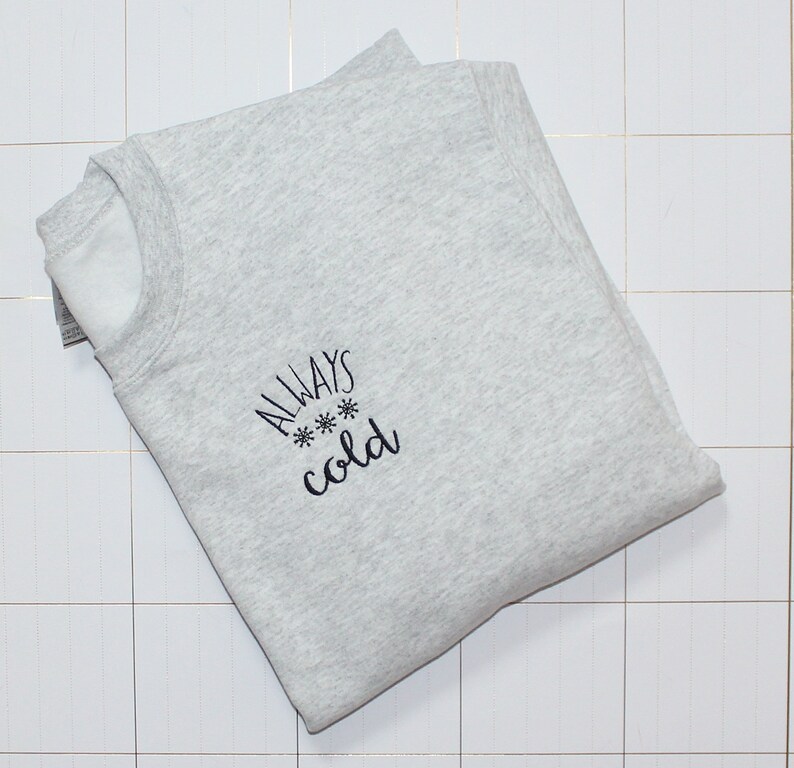 Pode incluir: Uma camisa de moletom cinza com o texto "ALWAYS *** cold" bordado na frente.