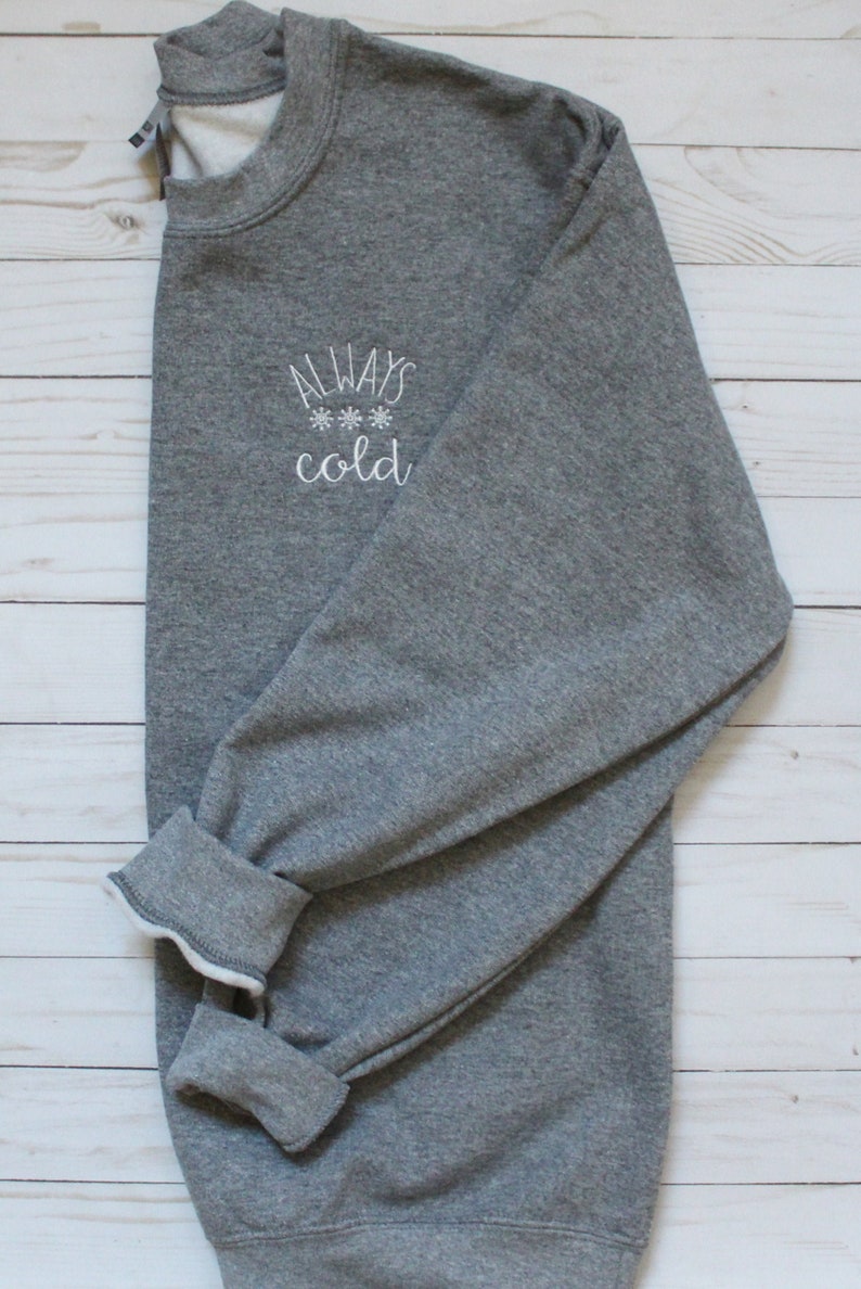 Pode incluir: Uma camisa de moletom cinza com o texto "ALWAYS *** cold" bordado na frente.