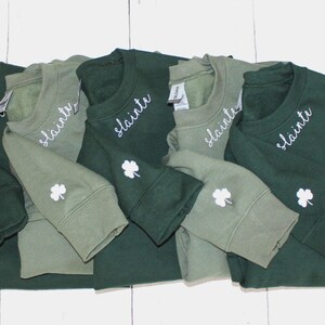 May include: Five green and olive green sweatshirts with the word "slainte" embroidered on the front and a shamrock embroidered on the sleeve.