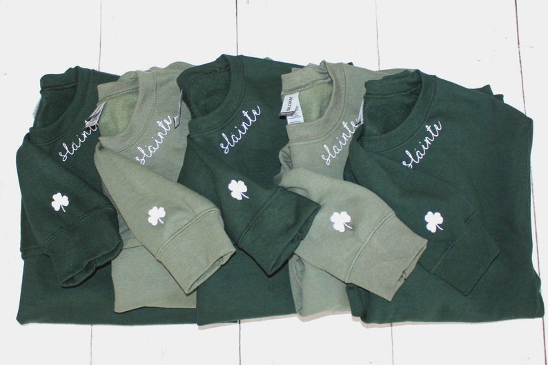 May include: Five green and olive green sweatshirts with the word "slainte" embroidered on the front and a shamrock embroidered on the sleeve.