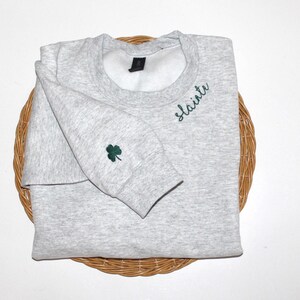 May include: A gray sweatshirt with a green shamrock embroidered on the sleeve and the word "slainte" embroidered on the front.