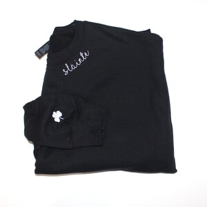 May include: Black sweatshirt with a white embroidered shamrock on the sleeve and the word "slainte" on the front.