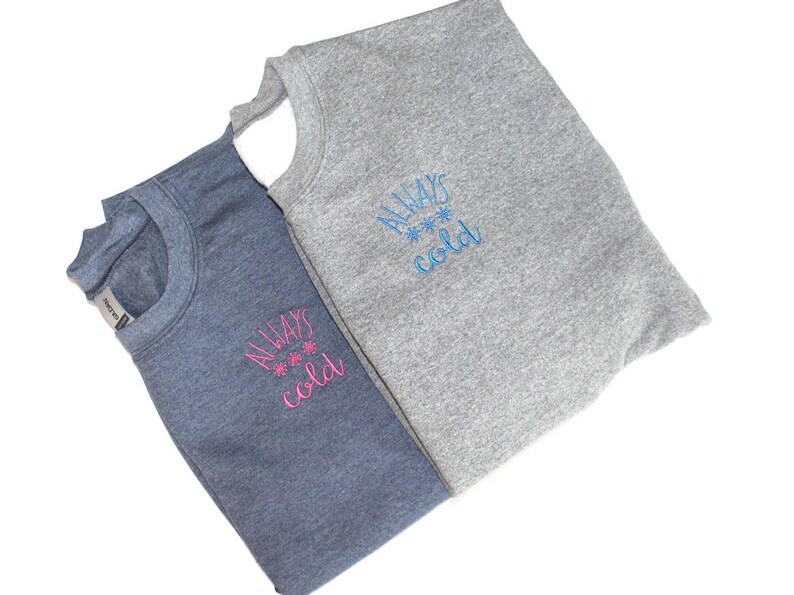 Pode incluir: Duas sweatshirts com o texto "ALWAYS cold" bordado na frente. Uma sweatshirt &eacute; cinza e a outra &eacute; azul. O texto &eacute; bordado em azul na sweatshirt cinza e em rosa na sweatshirt azul.