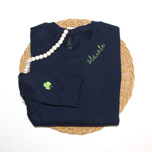 May include: A navy blue sweatshirt with a green shamrock on the sleeve and the word "slainte" embroidered on the right shoulder.
