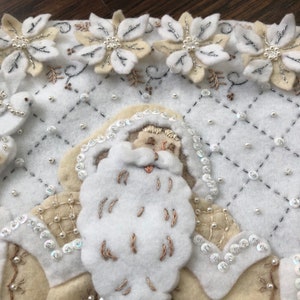 Puede incluir: Calcet&iacute;n de Navidad de fieltro blanco con una cara de Pap&aacute; Noel de fieltro blanco, bordada con hilo blanco. El calcet&iacute;n est&aacute; decorado con lentejuelas y cuentas blancas y plateadas.