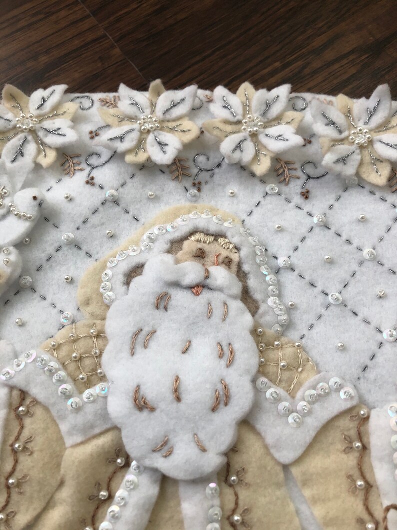 Puede incluir: Calcet&iacute;n de Navidad de fieltro blanco con una cara de Pap&aacute; Noel de fieltro blanco, bordada con hilo blanco. El calcet&iacute;n est&aacute; decorado con lentejuelas y cuentas blancas y plateadas.