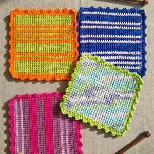 May include: Four colourful, square crochet washcloths. One is green with orange stripes and an orange scalloped edge. Another is blue with white stripes and a blue scalloped edge. The third is pink with purple stripes and a pink scalloped edge. The fourth is a mix of blue, green, and white with a green scalloped edge.