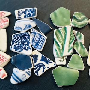 May include: Assortment of colorful ceramic tile pieces. The tiles are broken into various shapes and sizes. Some tiles feature a blue and white floral pattern, while others have a red and white floral pattern. There are also green and yellow tiles with abstract designs.