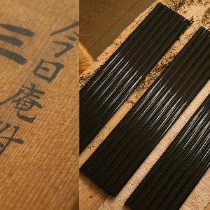 May include: A close-up of a wooden surface with Japanese characters and several sets of black chopsticks. The chopsticks are arranged in parallel lines, suggesting they are for dining.