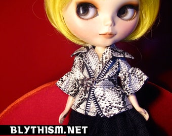 May include: A doll with yellow hair wearing a black and white patterned jacket and a black skirt. The doll has blue eyes and is wearing a black and white patterned jacket and a black skirt. The doll is sitting on a red surface.