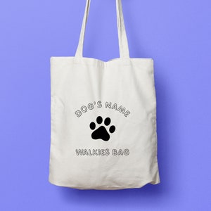 Puede incluir: Bolsa de lona blanca con texto negro que dice "DOG'S NAME" con una huella de pata negra en el centro y "WALKIES BAG" debajo de la huella de pata.