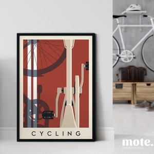 May include: A framed poster with a cycling theme. The artwork features a bicycle illustration in cream and red, with the word "CYCLING" at the bottom. Another framed poster is visible on the left. The room has a white sofa and a bicycle.