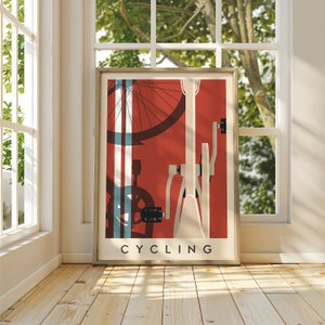 May include: Framed poster with a cycling theme. The artwork features a bicycle illustration in white and black against a red background. The word "CYCLING" is printed in black at the bottom of the poster. The poster is displayed in a room with natural light.